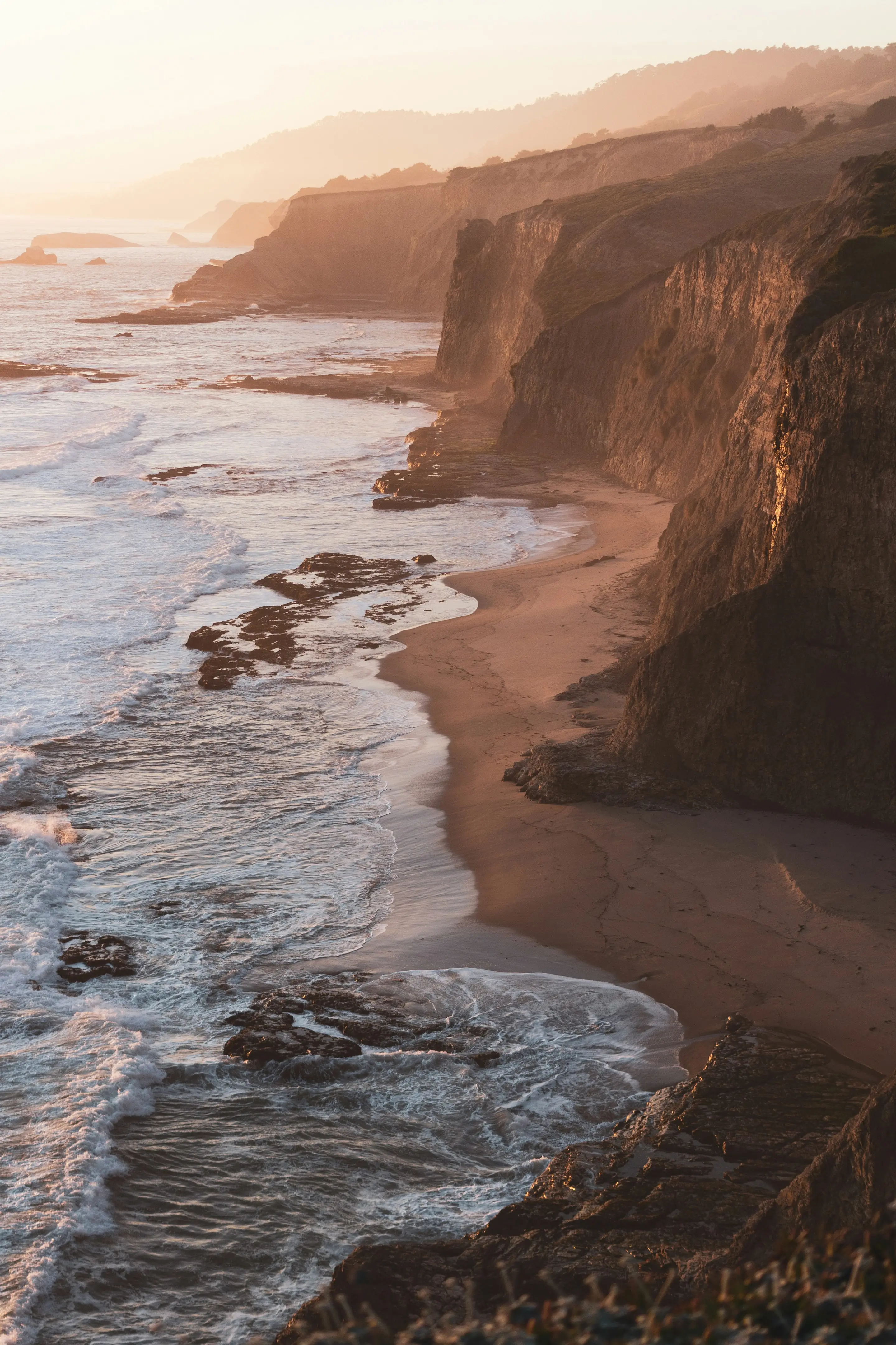 Waves washing onto an empty beach below a coastal cliff