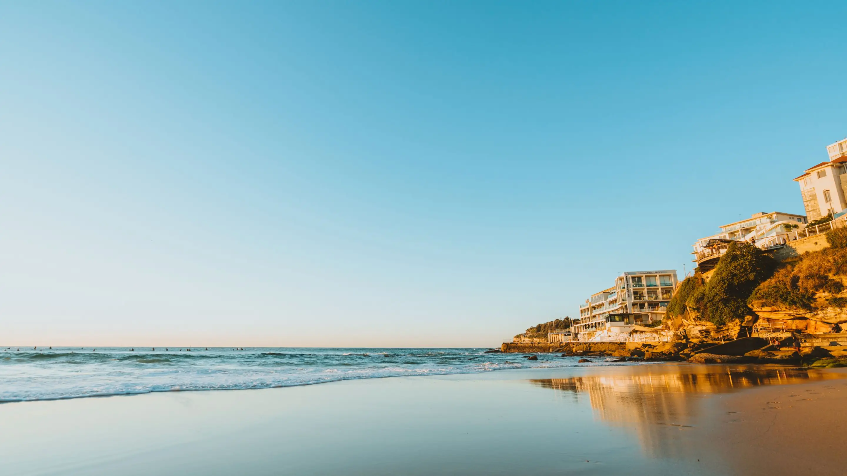 Sunlit shallow water along the California coast, with homes on the bluff above